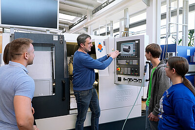 Dozent bedient Maschine über Bildschirm und Studierende sehen ihm zu