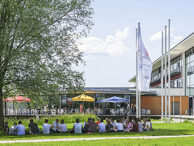 Studierende in der Wiese sitzend vor dem Gebäude A am Campus Hof