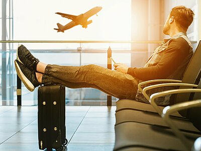 Mann wartete am Flughafen mit seinen Beinen auf dem Koffer.