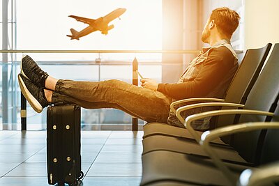 Mann wartete am Flughafen mit seinen Beinen auf dem Koffer.