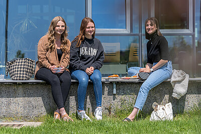 3 Studentinnen sitzen vor dem A-Gebäude der Hochschule Hof