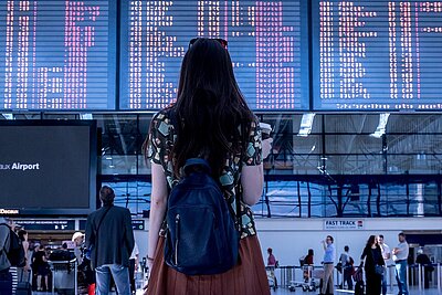 Frau steht vor Flughafen-Anzeigetafel