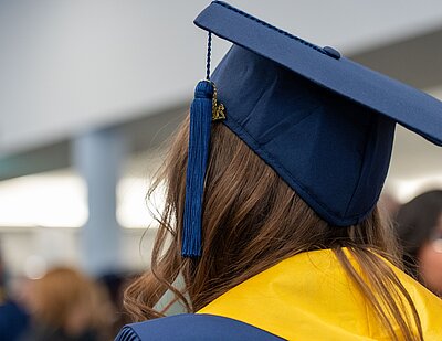 Absolventin mit Talar und Doktorhut in den Farben blau und gelb