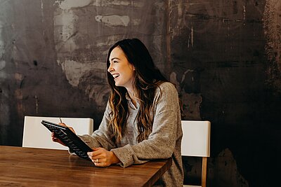 Studierende mit dunklen langen Haaren sitzt am Tisch und blick auf das Tablet