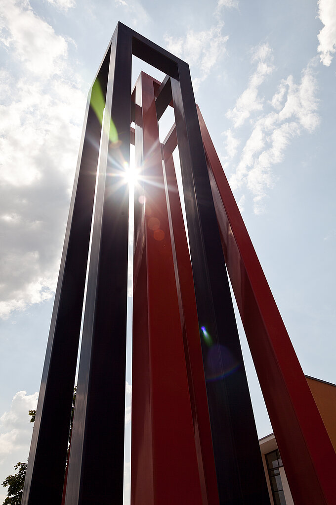 Architektur: Rot-blaue Säule am Campus Hof mit Sonne, die hindurch scheint
