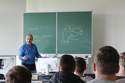 Lehrender vor Tafel mit einem Kurs Studierender